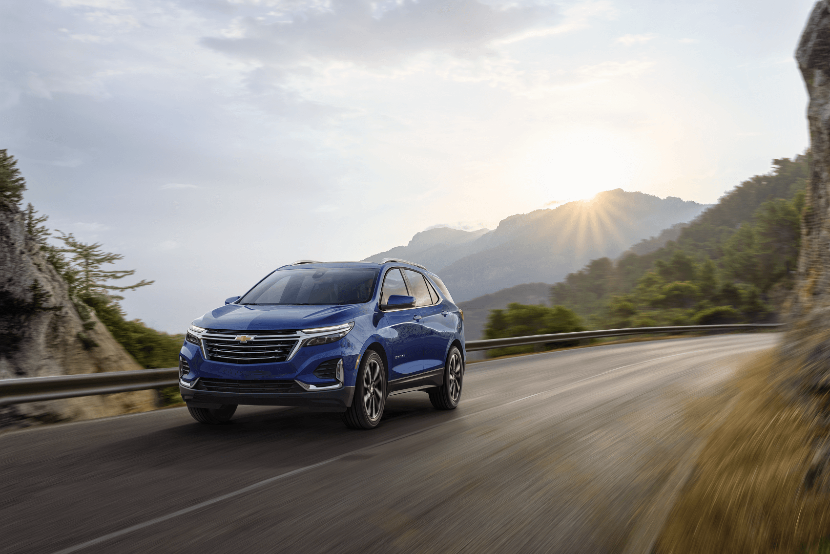 blue chevy equinox drives down road with mountain view in the background